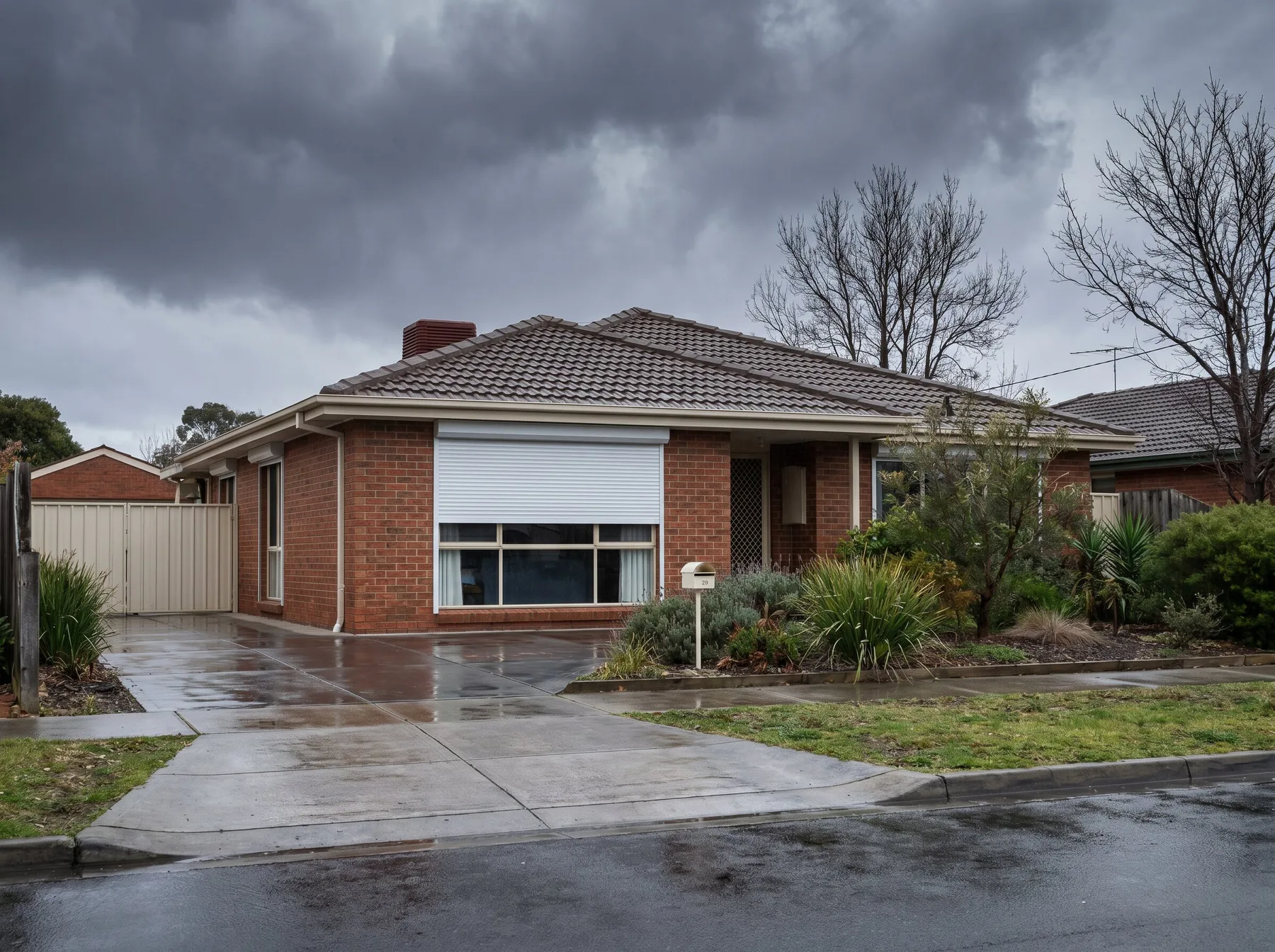 A white aluminium roller shutter three-quarters closed over a street-facing window as storm clouds build